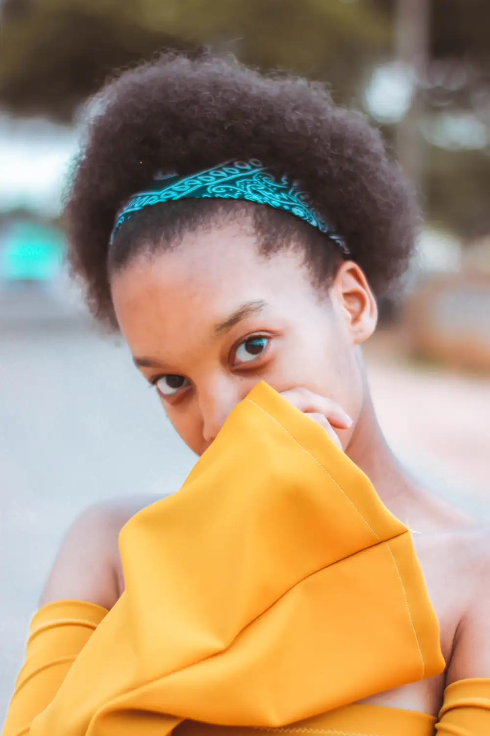 Pretty beige-skin girl with afro hair held by bandana wearing a yellow  dress cover her mouth while giving a fierce look