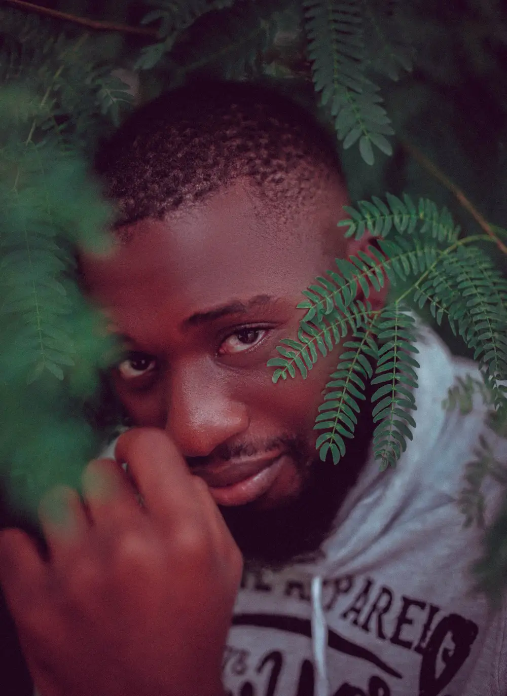 Man posing stylishly behind a green tree