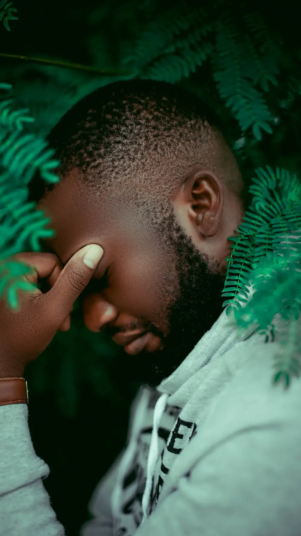 Man posing stylishly behind a green tree