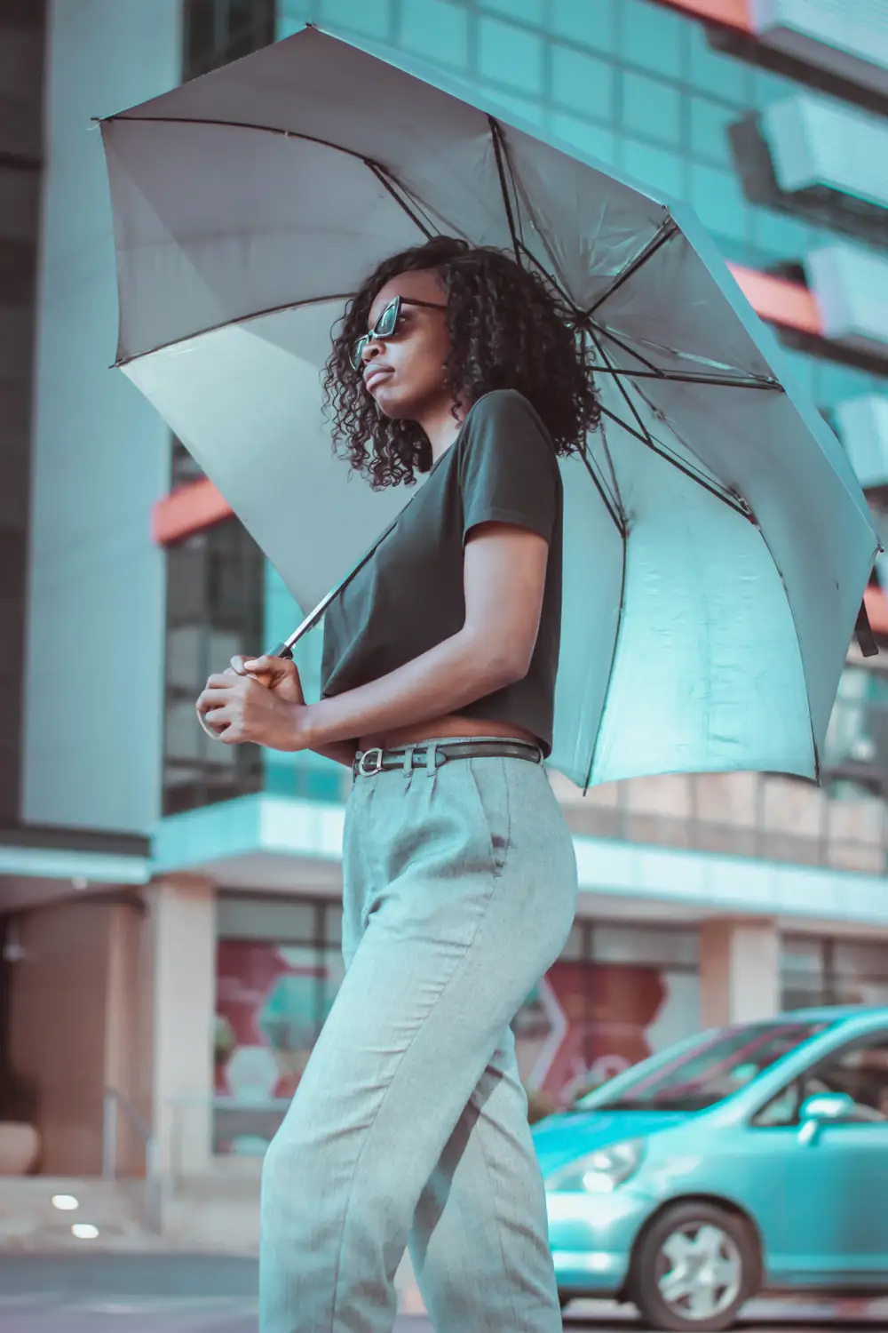 Black girl wearing a black crop top, black eye glasses and spread an umbrella