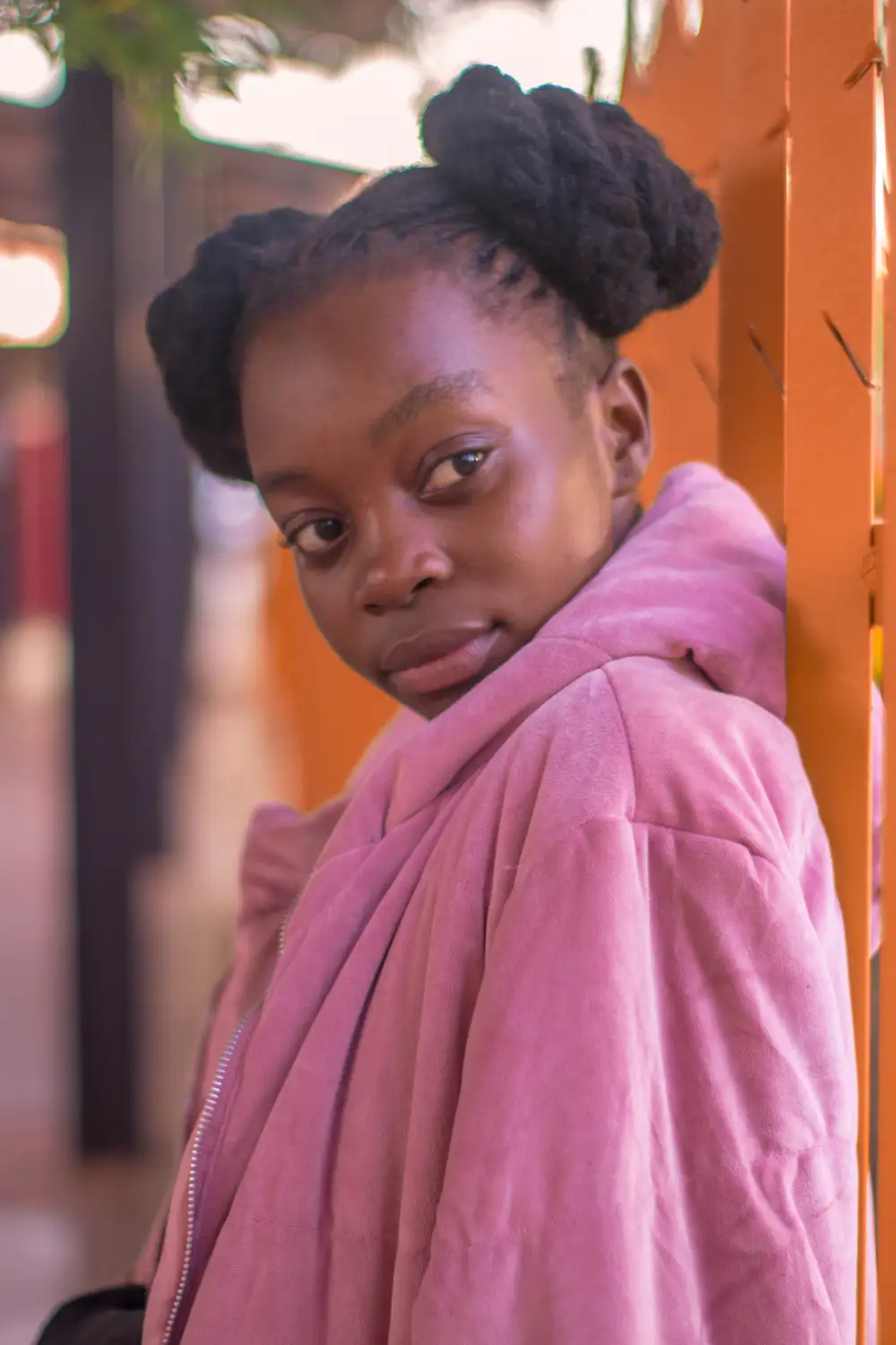 Black girl on braids wearing a cardigan jacket and leaning on a gate