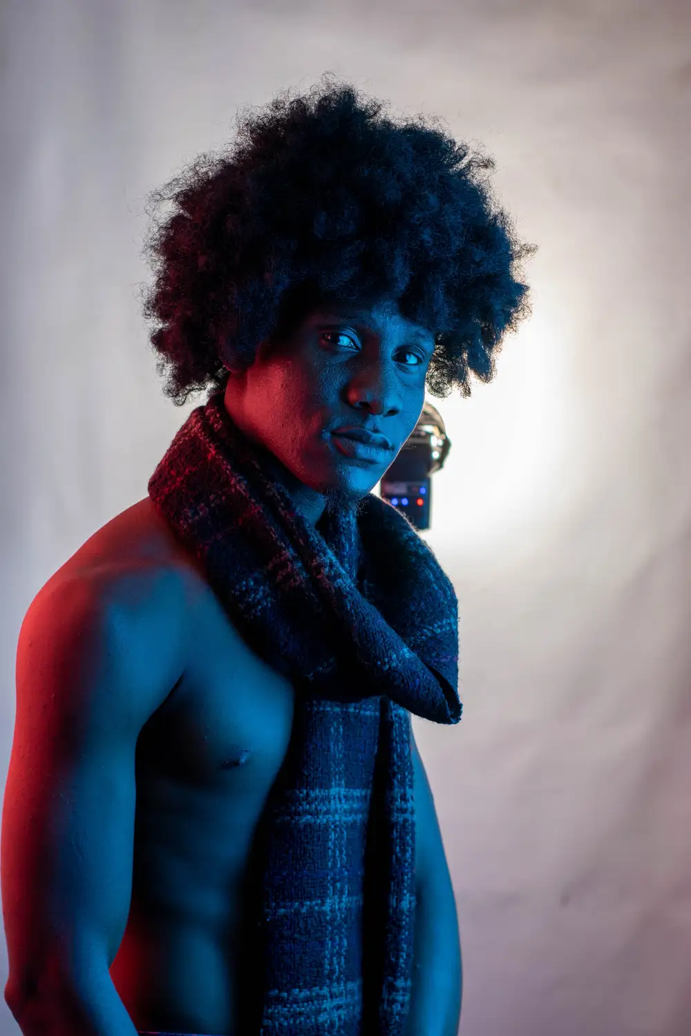 model with afro hairstyle has a scarf around his neck and looks at the camera