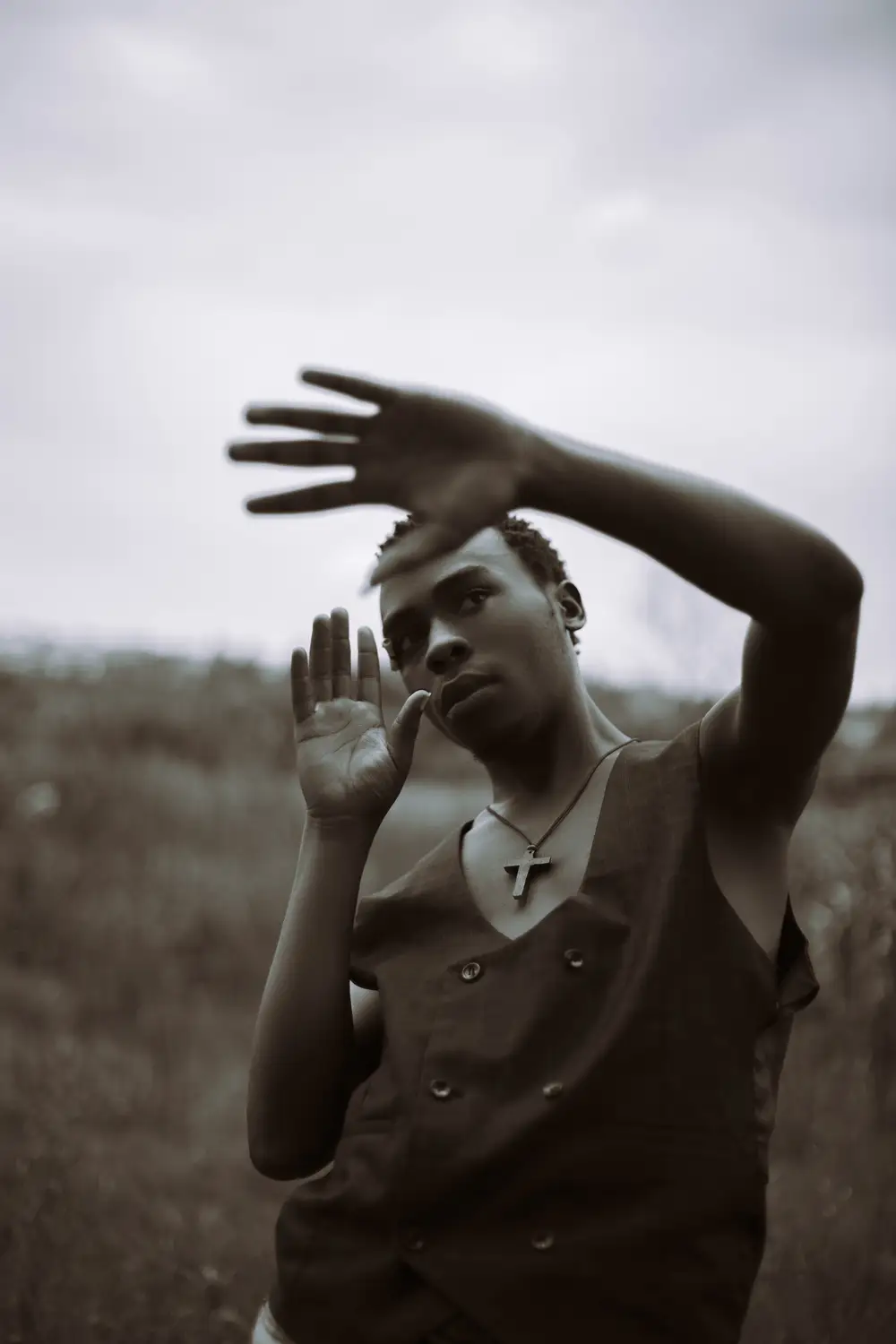 Man with hands above eye level with a cross on neck