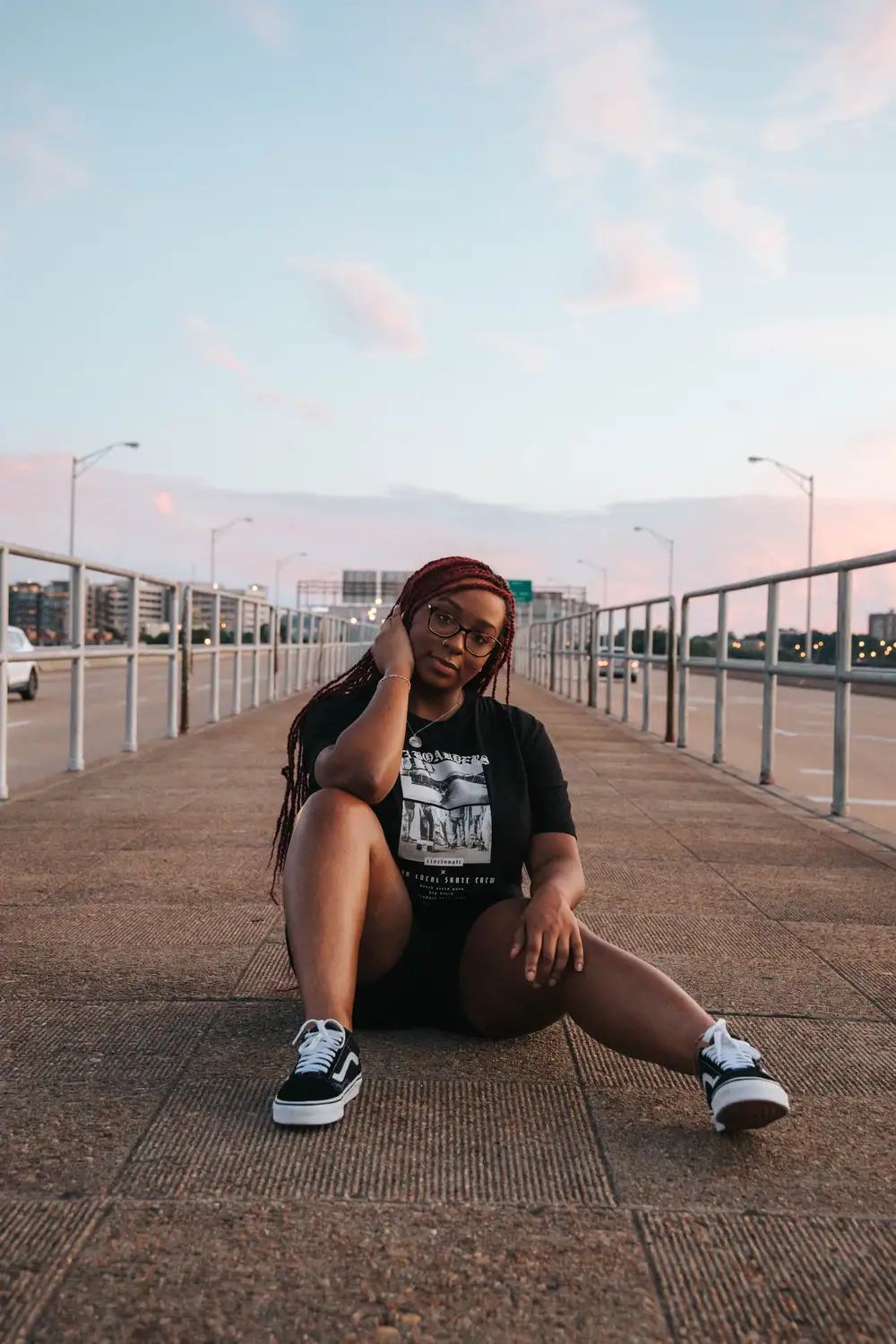 Lady on braids wearing black shirt and sitting on the road