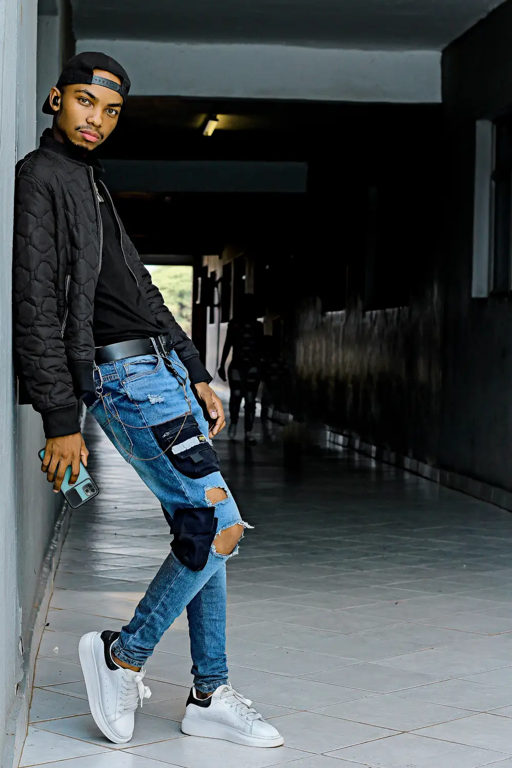 Young boy with ripped jeans and face cap posing with the wall on a walkway
