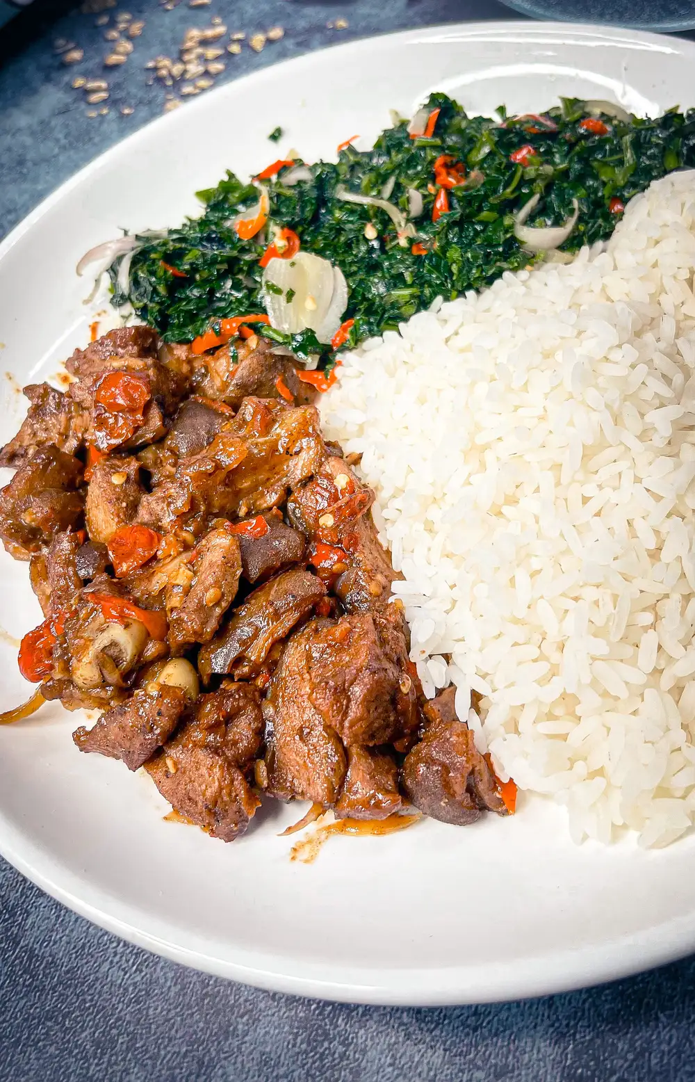 Deeply sauced and grilled goat meat with rice served with ugwu sauteed