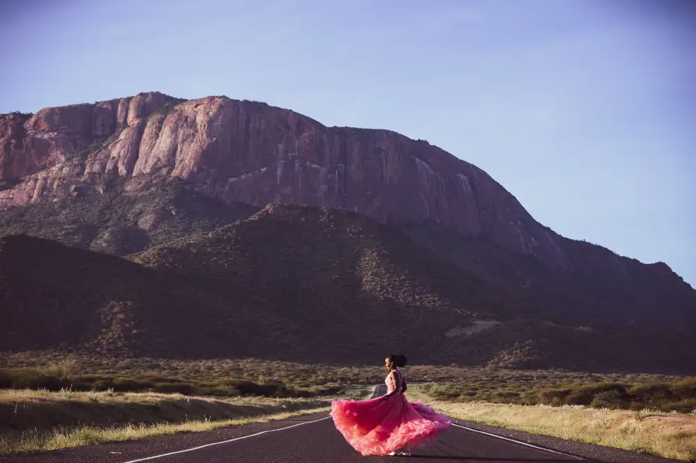 Woman wearing a pink dress on a road path leading to a mountain