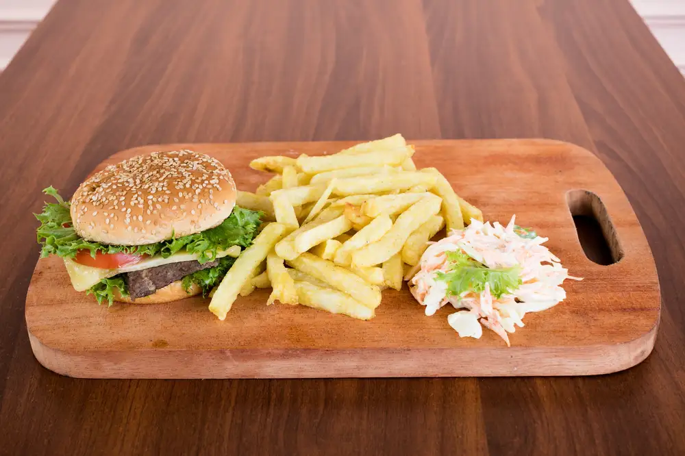 Burger and potato fries with salad on a wooden board