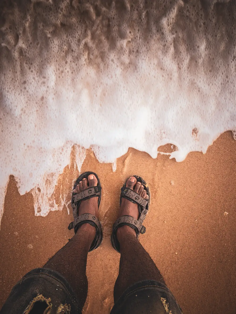 Person with sandals standing on beach sand