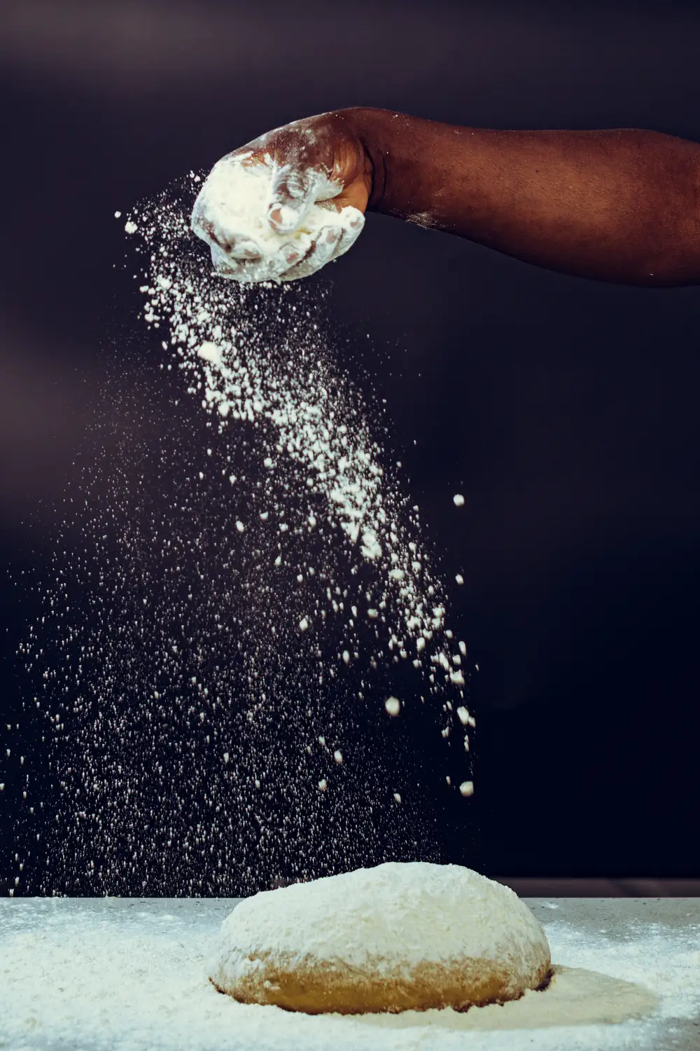 Baker sprinkling flour for dough kneading
