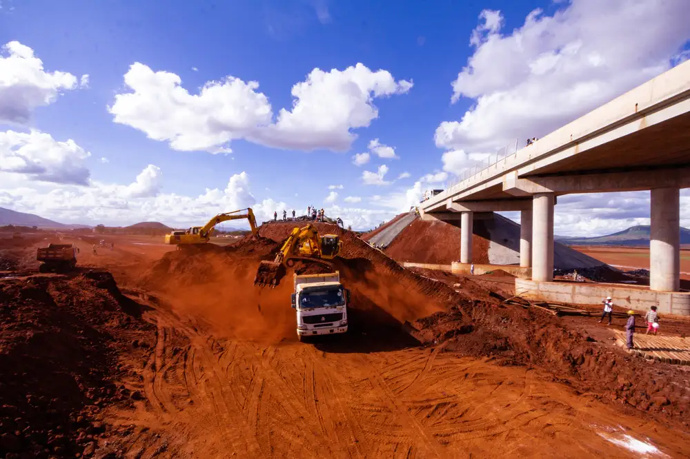 Truck offloading red sand at a bridge construction site