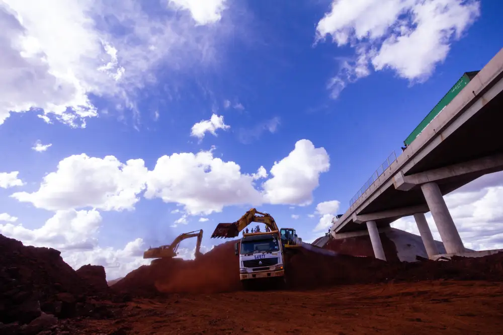 Truck offloading red sand at bridge construction site