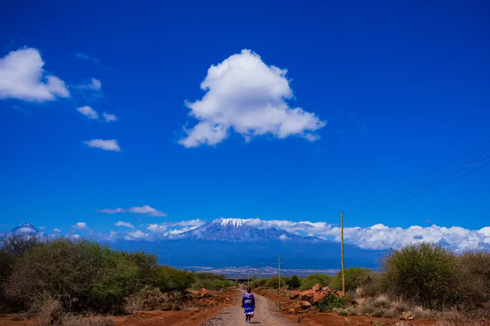 woman on traditional attire walking through a road path with mountain and sky background