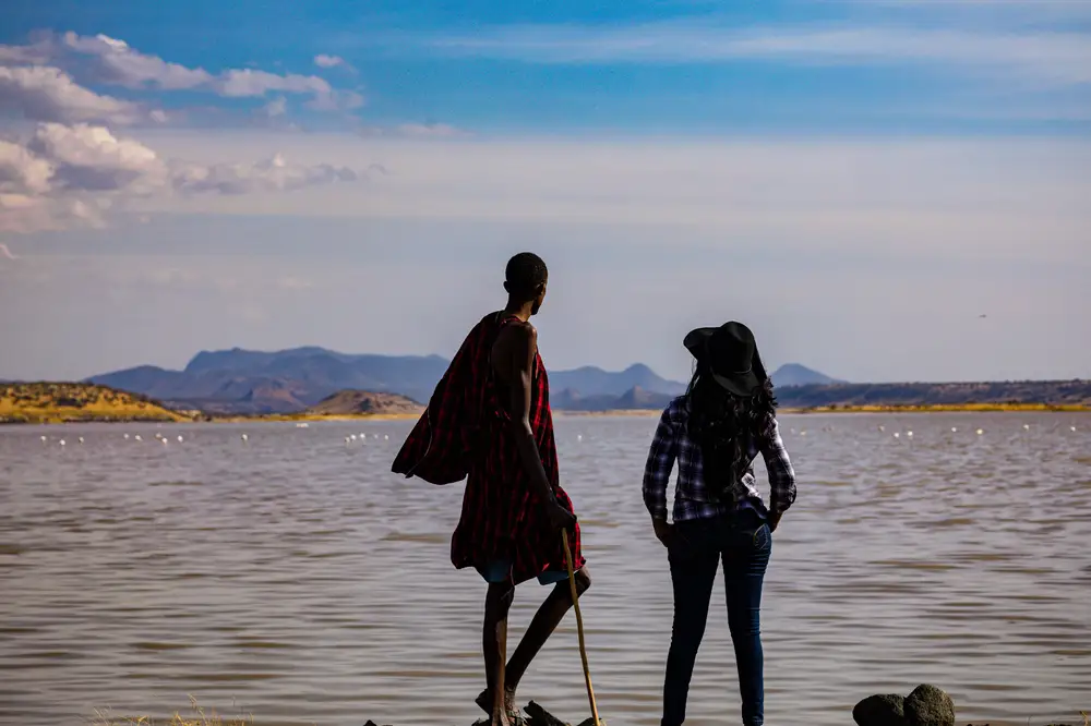 Indigenous man and Cowgirl standing by a lake