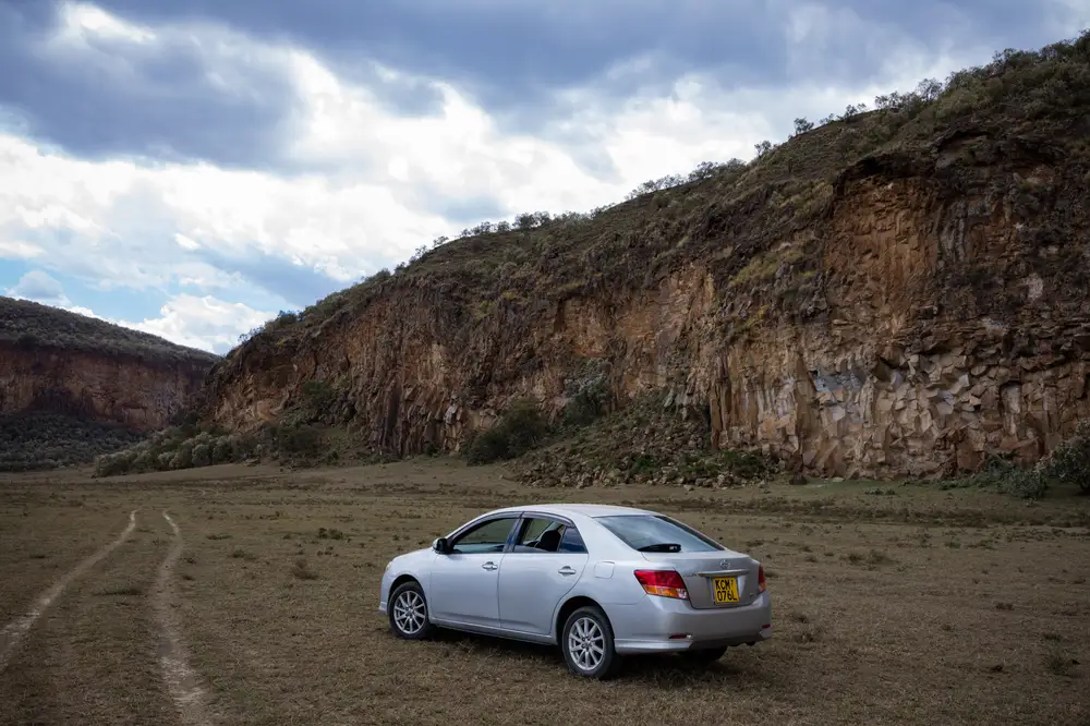 Silver colored car beside a large hill