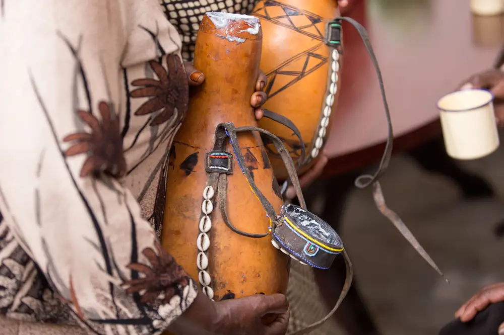 Woman holding a gourd of palmwine decorated with Cowries
