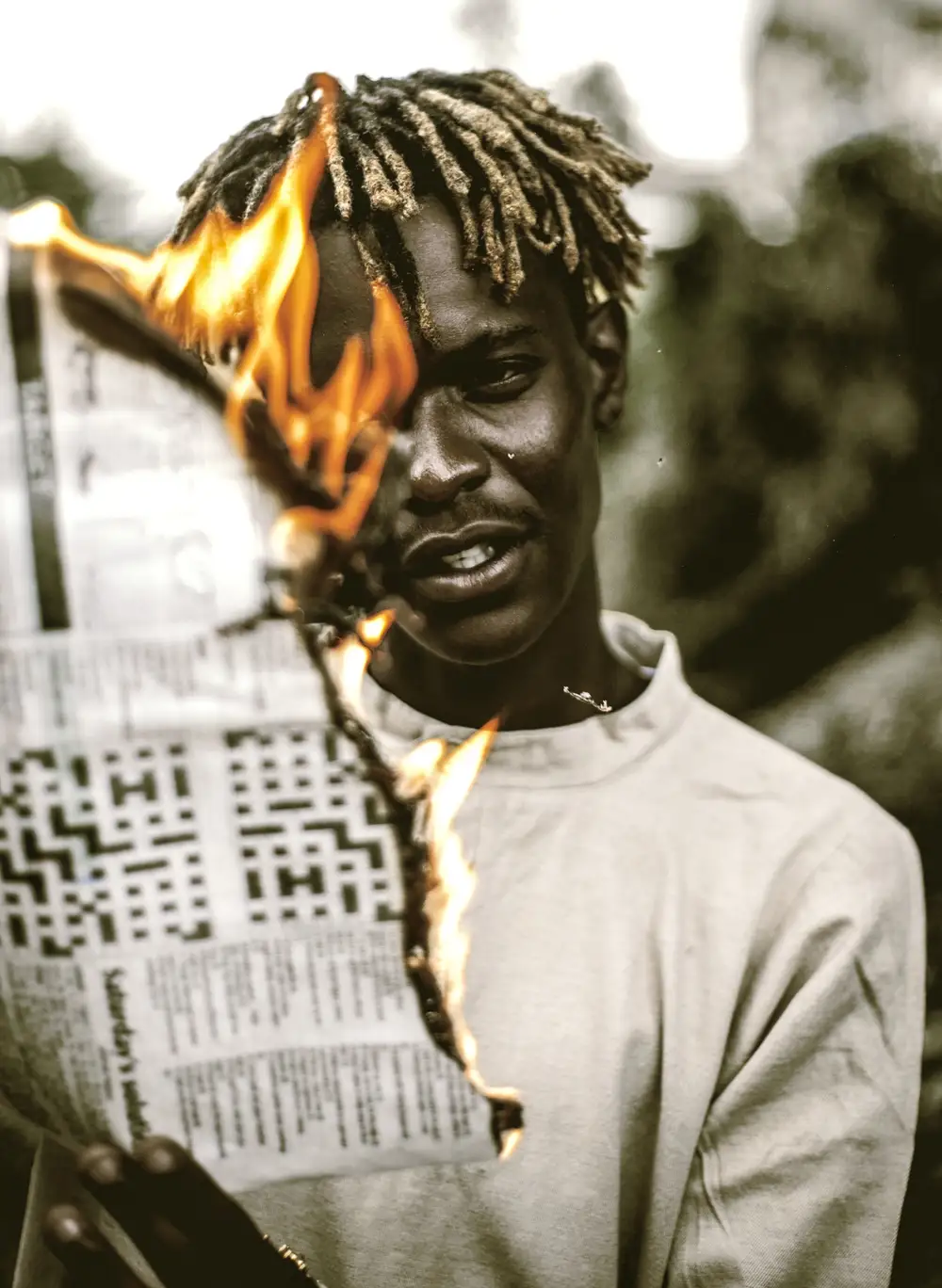 Man in dreadlocks holding a burning Newspaper