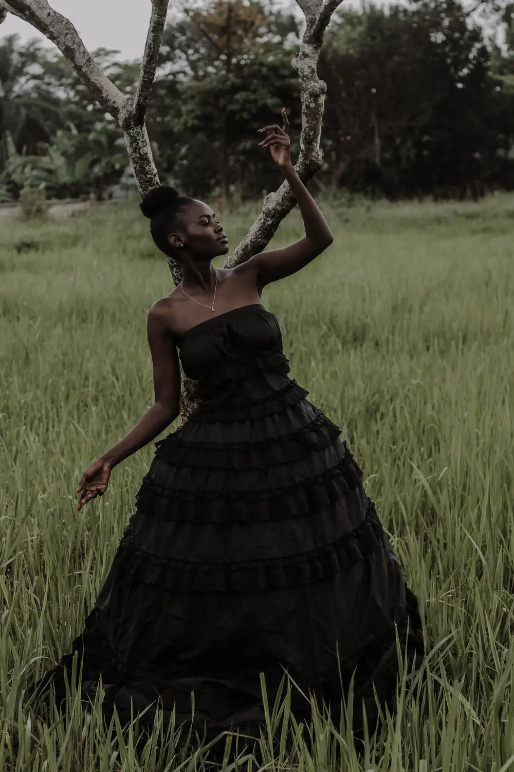 Woman in Black Dress Standing Beside a Bare Tree