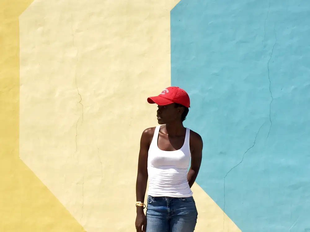 Lady rocking a red cap and denim standing in front of a colored wall