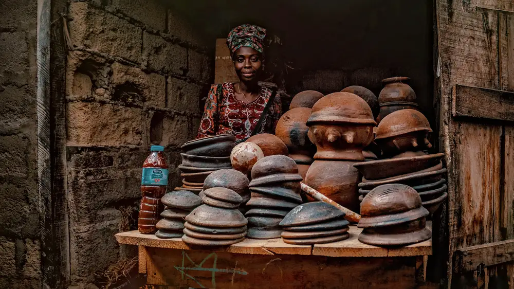 woman selling clay and ceramic pots on a wooden table poses with her wares