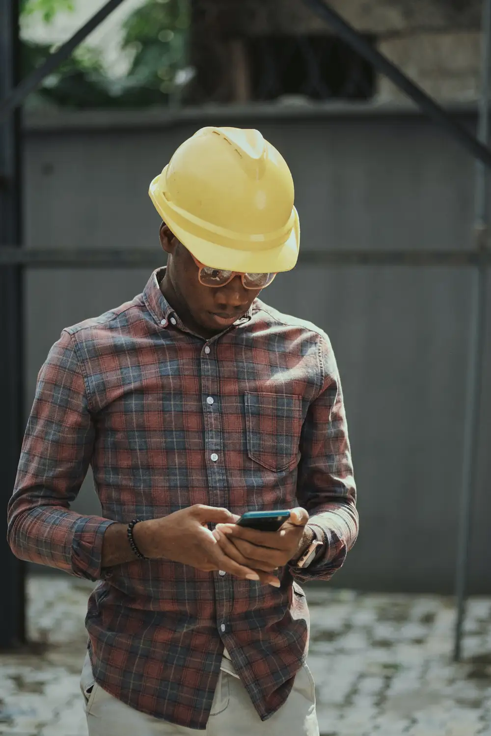 Portrait of a black man architect at a building site looking at camera. Confident civil engineering wearing a hardhat and eye goggles.