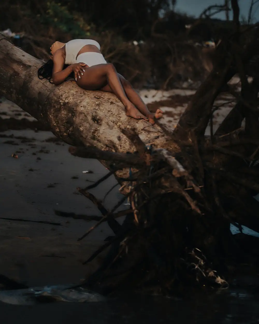summer photo of a sunbathed African woman lying on a fallen branch at a summer beach with white sand and big sea waves.