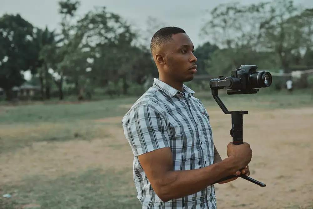 Filmmaker in Blue and White Plaid Button Up T-shirt Holding Black Dslr Camera on a gimbal.