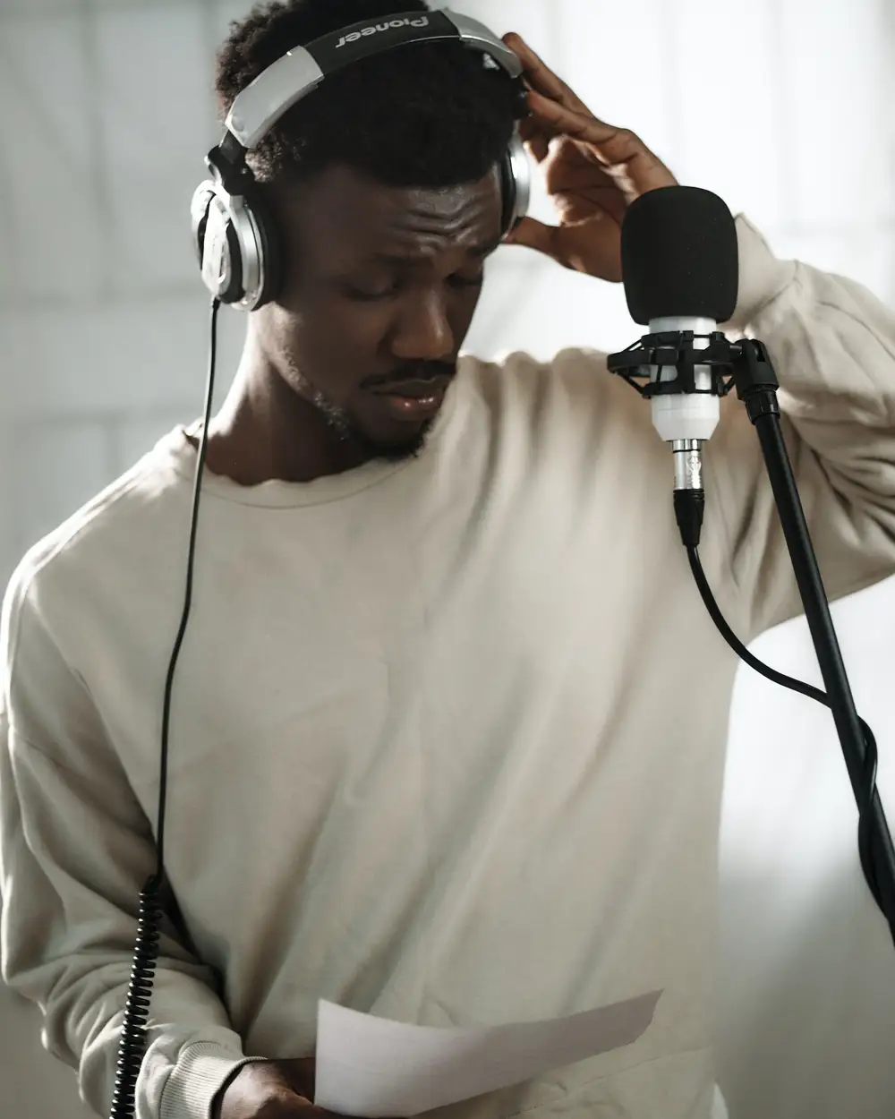African male voice over artist recording a voice-over script with a condenser and Pioneer exclusive headphones.