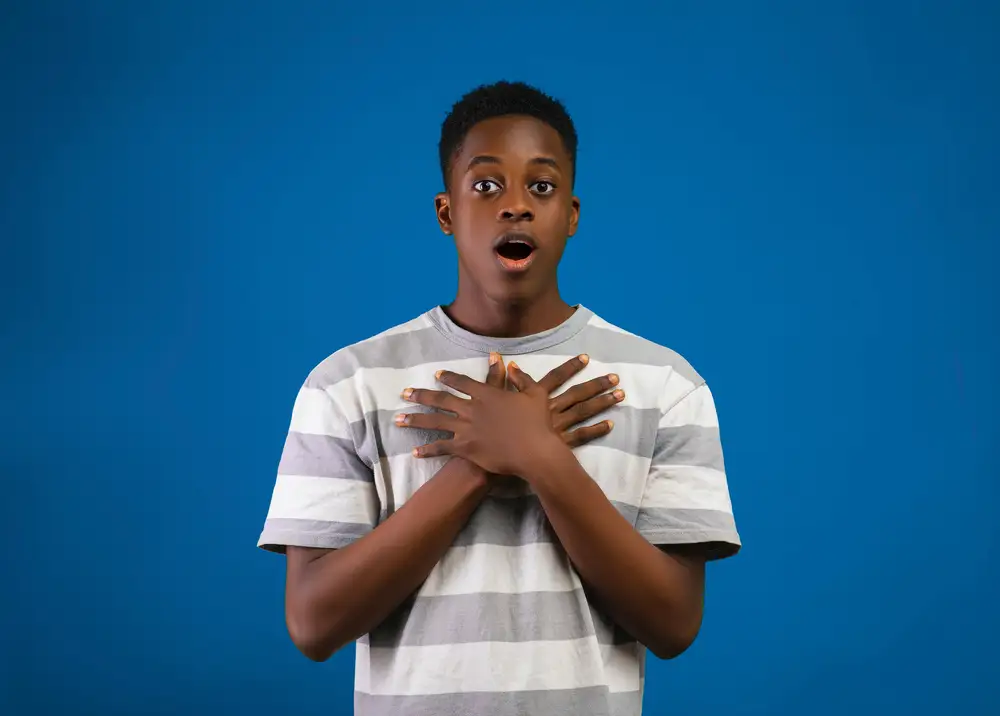young man holding his chest with shocked expression