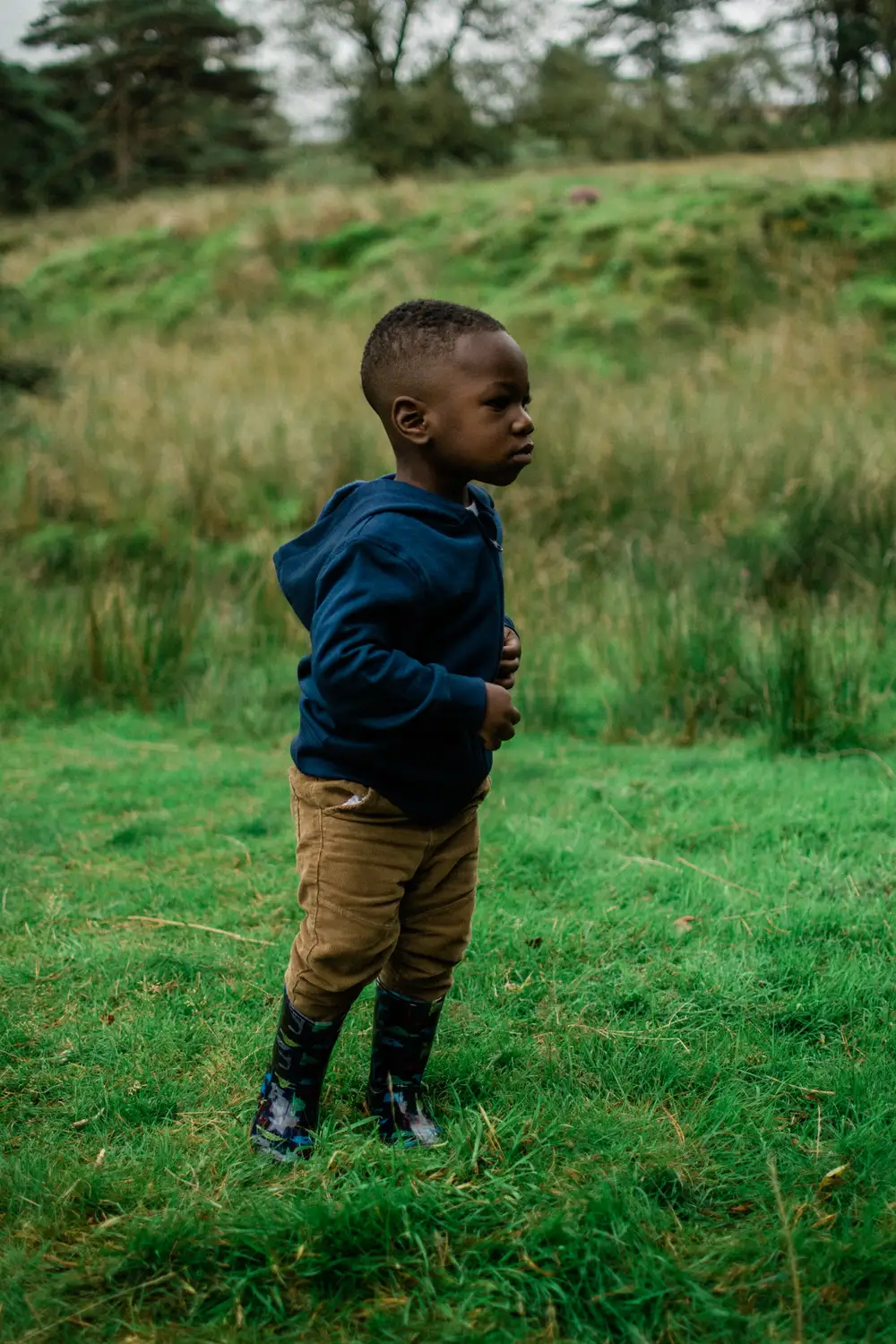 Toddler in boots standing in a grass field