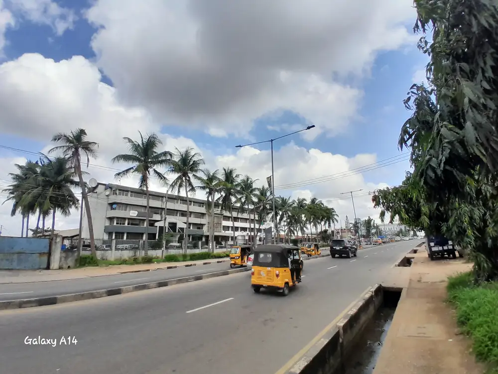 scenic road lined with palm trees and buildings. It captures an outdoor setting with a clear sky and some clouds. with moving vehicles